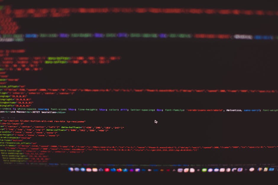 A person working on a laptop with a dark screen displaying lines of code in various colors, including green, white, and blue. The laptop is positioned on a black desk or table, with the person's hands